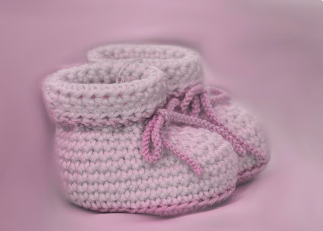 Sapatinhos de bebê em crochê rosa com cadarço, sobre fundo rosa