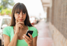 Mulher segurando celular com expressão de dúvida em ambiente urbano