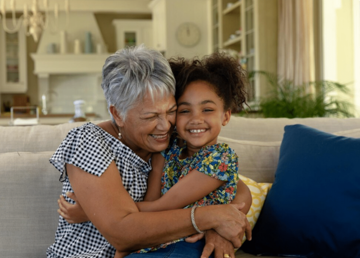 Avó abraçando a neta com carinho e alegria no sofá de casa.