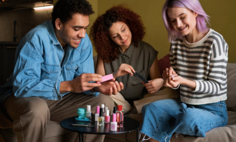 Três pessoas se divertem fazendo as unhas juntas com esmaltes e acessórios sobre a mesa.