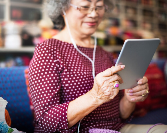 Idosa sorrindo enquanto usa tablet com fones de ouvido, em ambiente acolhedor