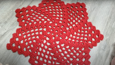 Centro de mesa em crochê vermelho com ponto aberto sobre superfície de madeira