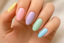 Unhas de esmalte pastel em tons suaves de amarelo, rosa, lilás, verde e azul, combinando com a tendência de cores delicadas e vibrantes.