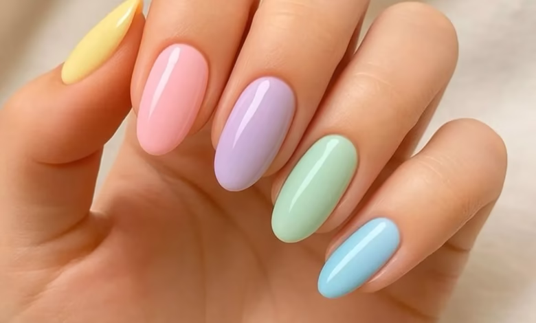 Unhas de esmalte pastel em tons suaves de amarelo, rosa, lilás, verde e azul, combinando com a tendência de cores delicadas e vibrantes.