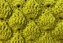 Detalhe de manta de crochê com ponto abacaxi em tom de amarelo, mostrando o relevo e a textura das camadas.