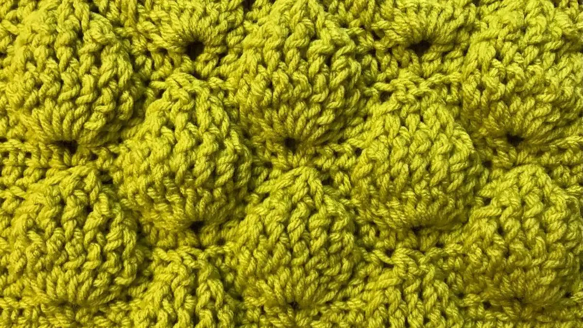 Detalhe de manta de crochê com ponto abacaxi em tom de amarelo, mostrando o relevo e a textura das camadas.