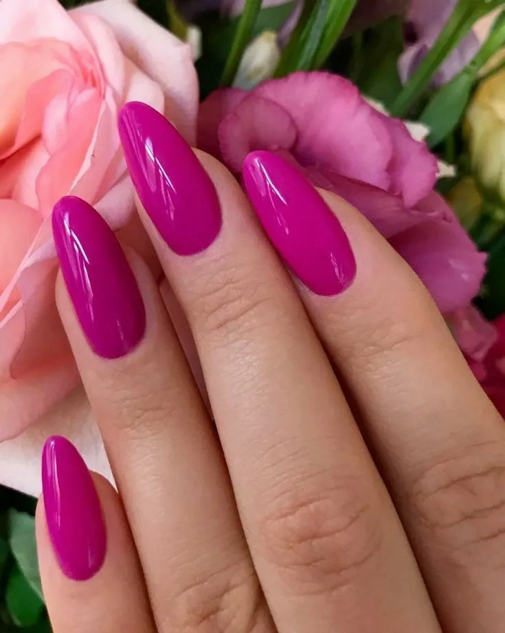 Unhas rosa fúcsia em fundo de flores suaves, representando a cor da atitude.