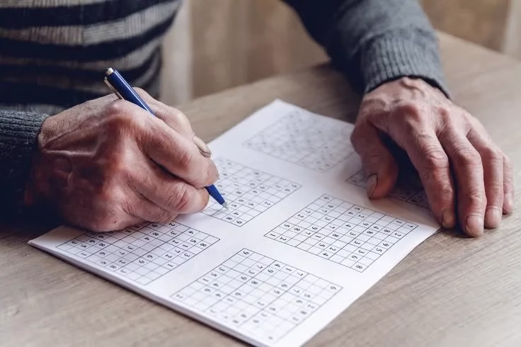 Idoso resolvendo um Sudoku com uma caneta, simbolizando a prática do exercício mental para melhorar a memória.