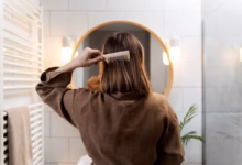 Mulher escovando cabelo em frente ao espelho, demonstrando um penteado rápido e simples.