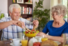 Casal idoso compartilhando uma refeição saudável com uma salada, simbolizando a importância de uma alimentação equilibrada para a saúde na terceira idade.
