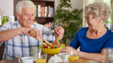 Casal idoso compartilhando uma refeição saudável com uma salada, simbolizando a importância de uma alimentação equilibrada para a saúde na terceira idade.