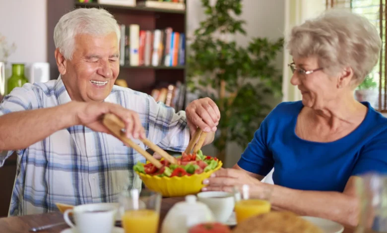 Casal idoso compartilhando uma refeição saudável com uma salada, simbolizando a importância de uma alimentação equilibrada para a saúde na terceira idade.