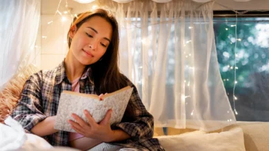 Mulher lendo um livro em um ambiente acolhedor com luzes suaves ao fundo, refletindo a calma e o relaxamento antes de dormir.