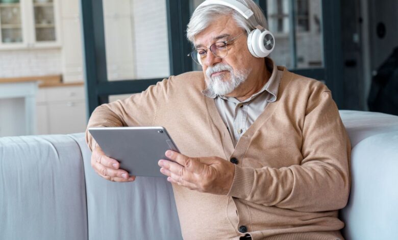 Idoso com fones de ouvido utilizando tablet para aprender com tecnologia