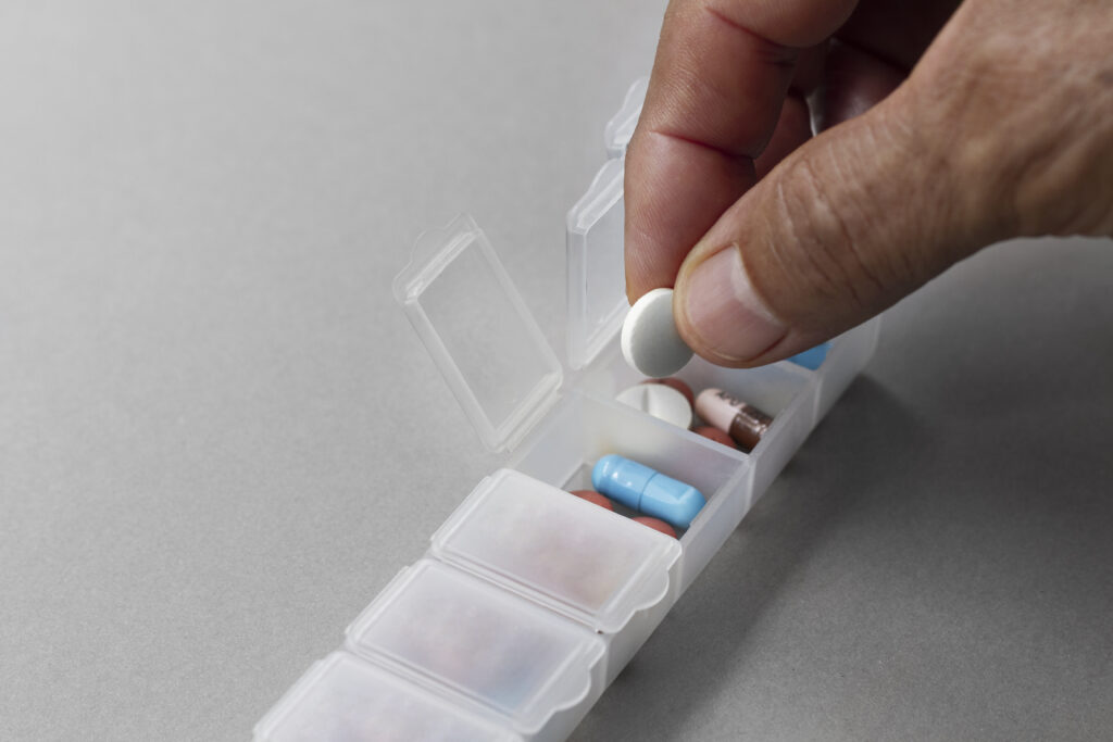  Mão organizando comprimidos em caixa de medicação semanal