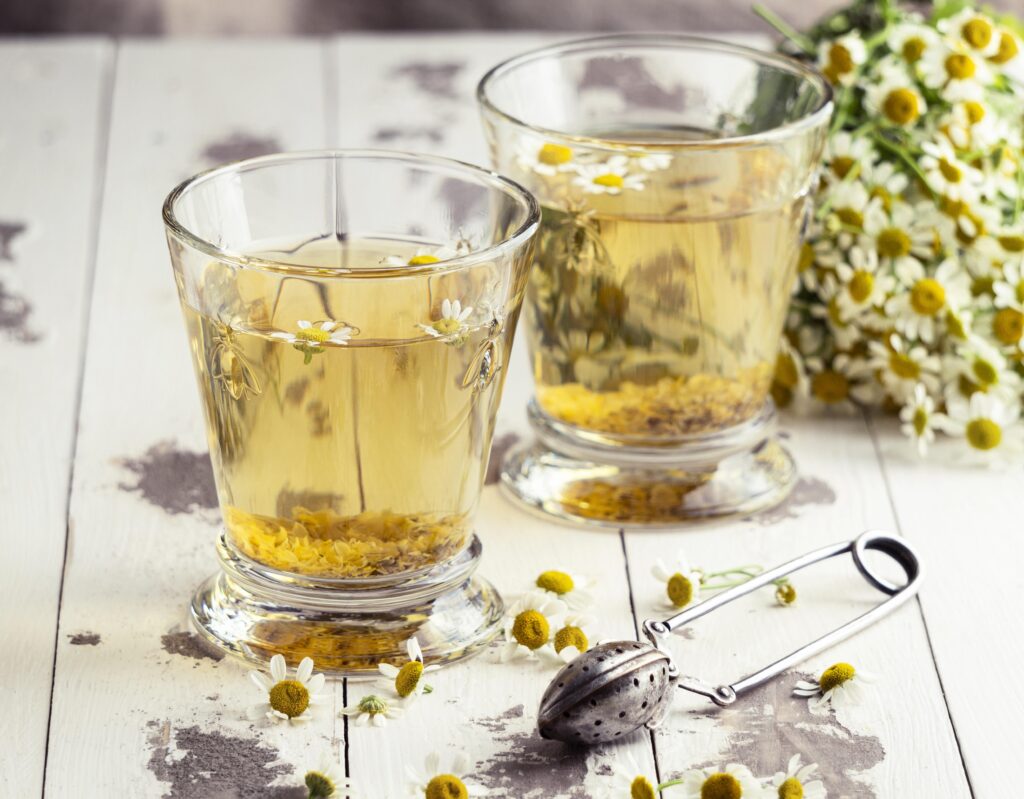 Chá de camomila servido em copos com flores frescas e infusor ao lado