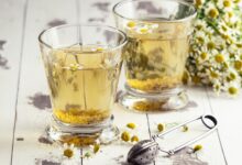 Chá de camomila servido em copos com flores frescas e infusor ao lado
