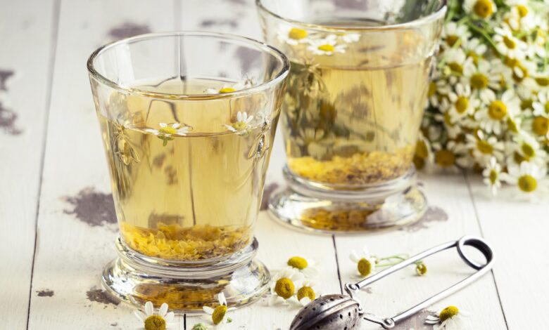 Chá de camomila servido em copos com flores frescas e infusor ao lado