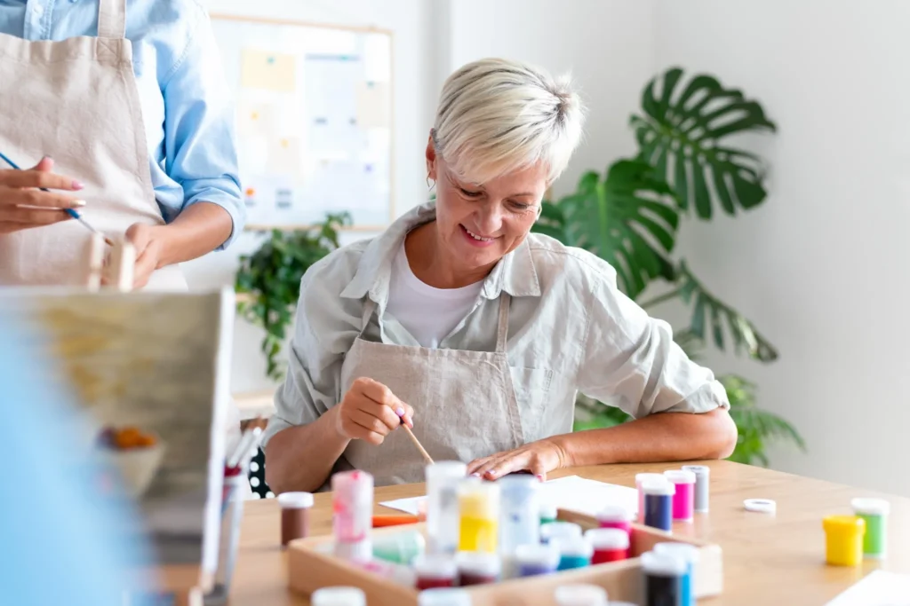 Pessoa mais velha pintando e praticando atividades manuais com materiais artísticos, como parte de um exercício terapêutico para melhorar a coordenação motora.