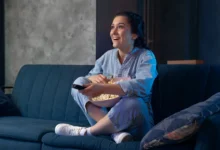Mulher jovem assistindo série ou novela turca em serviço de streaming, com uma tigela de pipoca nas mãos.