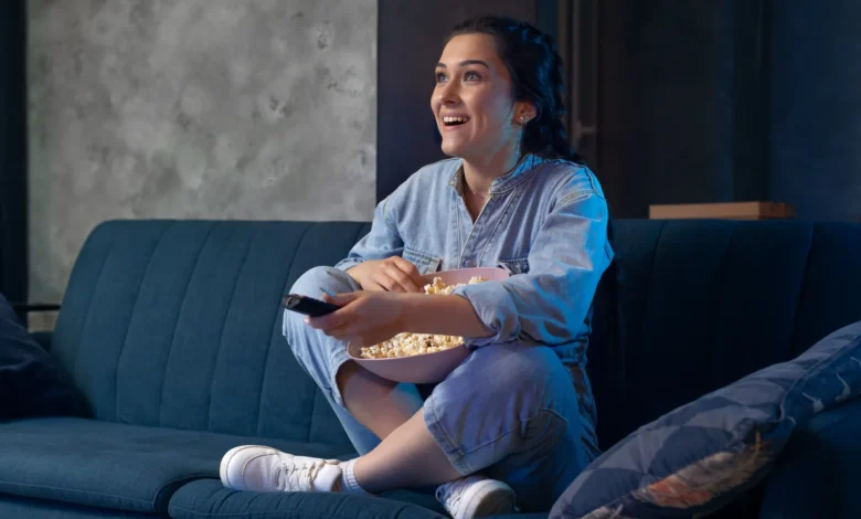Mulher jovem assistindo série ou novela turca em serviço de streaming, com uma tigela de pipoca nas mãos.