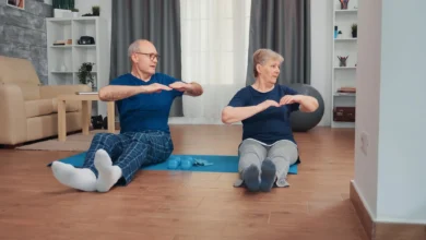 Casal idoso praticando exercícios juntos em casa, sentados em tapete de yoga para manter a saúde e a independência.