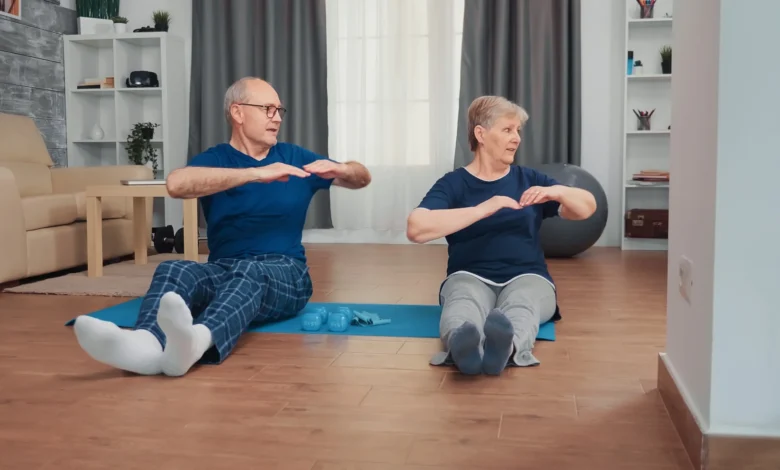 Casal idoso praticando exercĂcios juntos em casa, sentados em tapete de yoga para manter a saĂșde e a independĂȘncia.