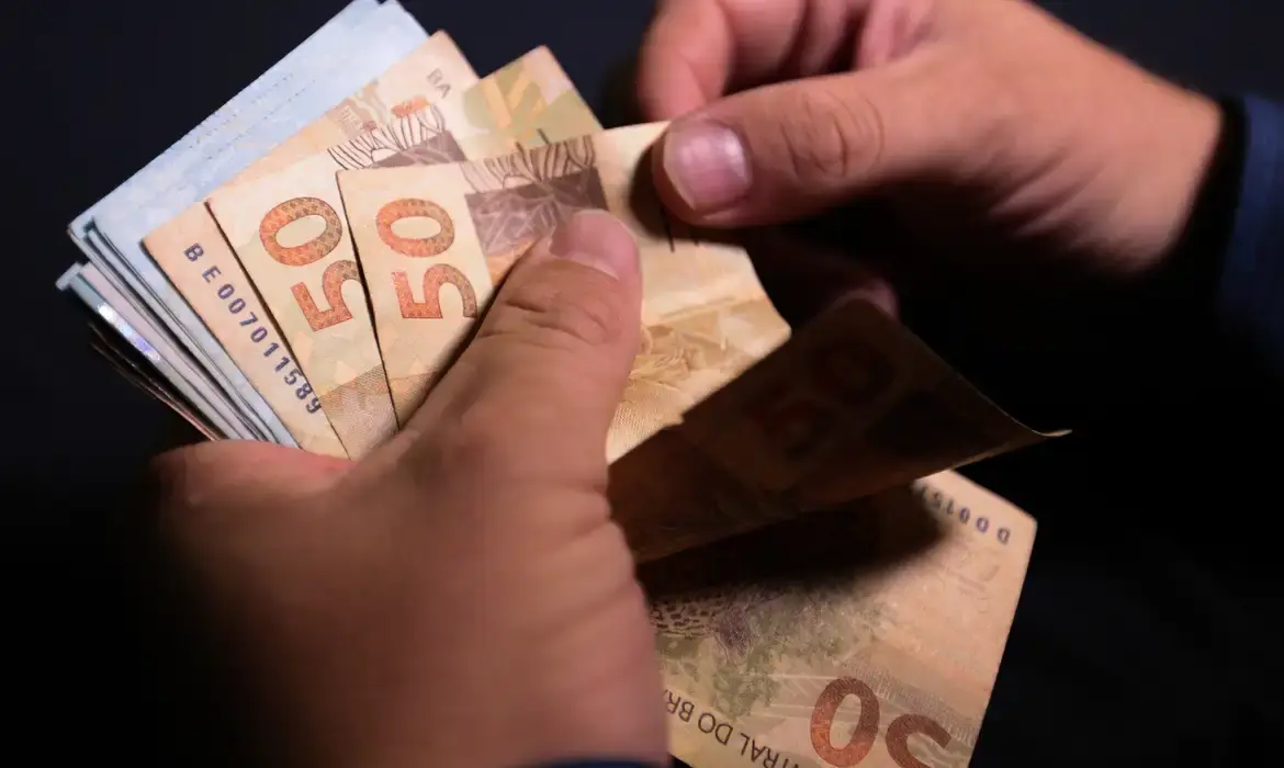 Pessoa contando notas de R$ 50 reais em ambiente escuro.