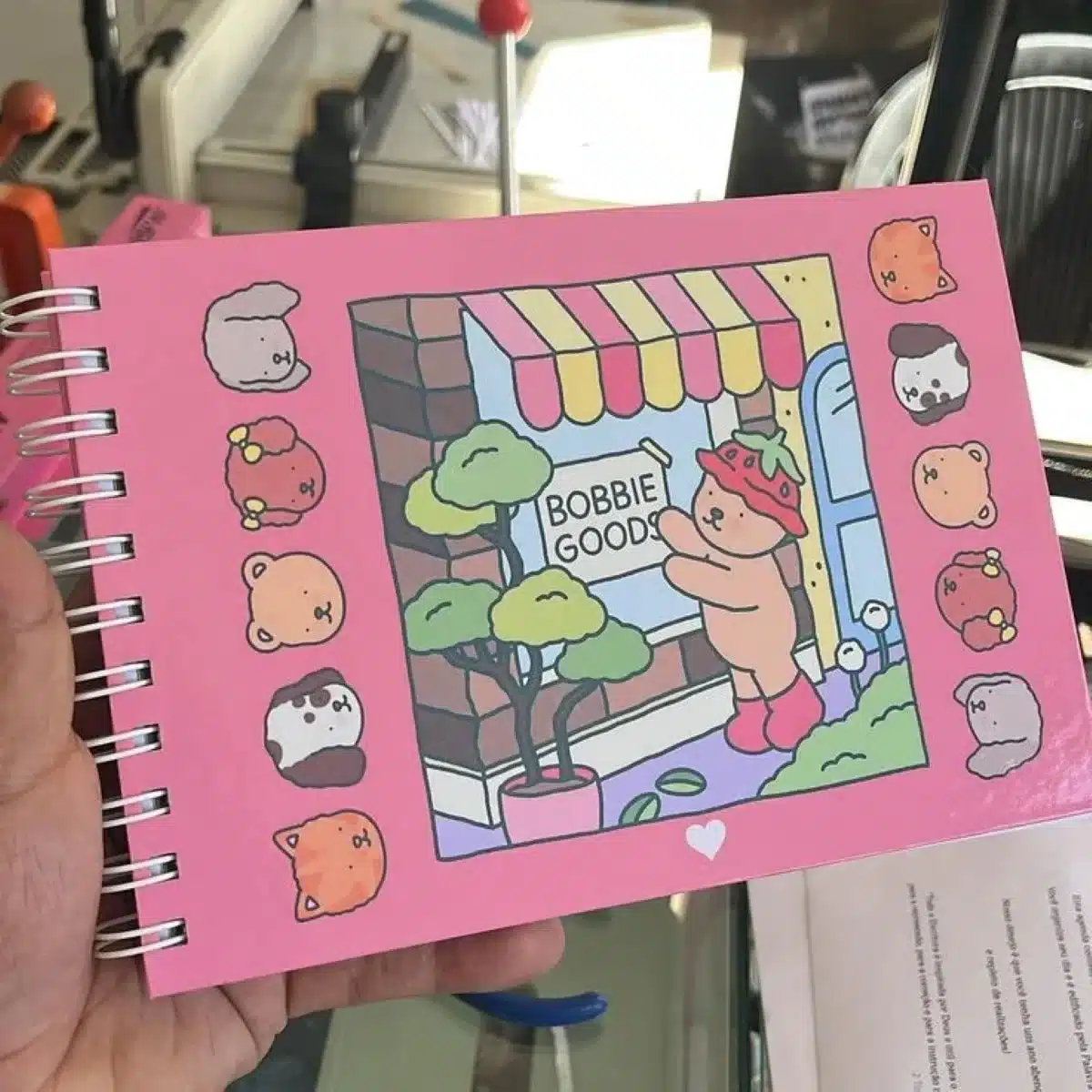 Desenho fofo de um ursinho vestido de morango em frente à loja Bobbie Goods, com personagens de animais ao redor