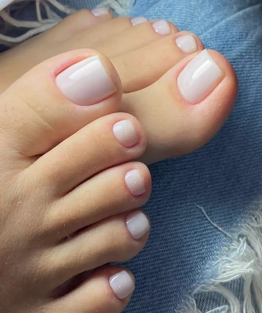 Unhas dos pés com esmalte branco translúcido, em um visual natural e suave.