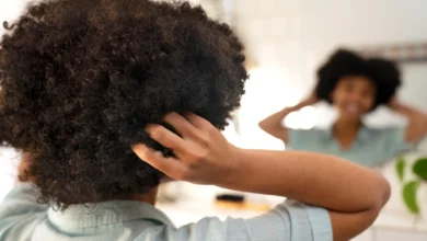 Mulher cuidando do cabelo afro, observando os cachos no espelho, destacando a importância dos cuidados durante a transição capilar.