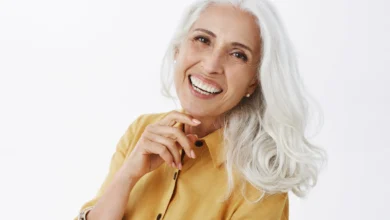 Mulher sorridente com cabelos brancos e elegantes, usando camisa amarela, mostrando confiança e estilo natural.
