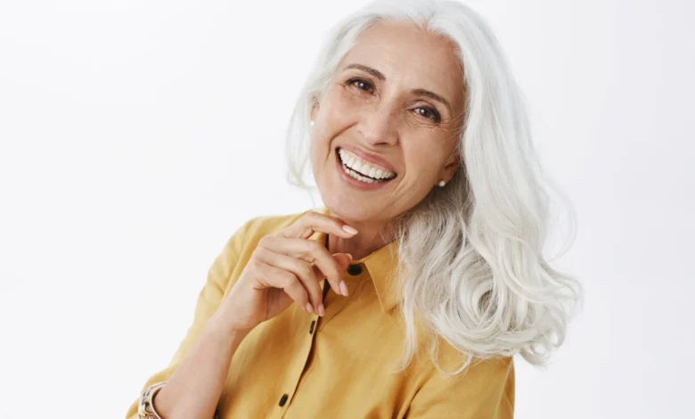 Mulher sorridente com cabelos brancos e elegantes, usando camisa amarela, mostrando confiança e estilo natural.