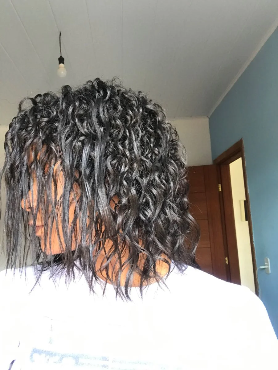 Mulher com cabelo cacheado em processo de transição capilar, exibindo cachos naturais em estilo médio.