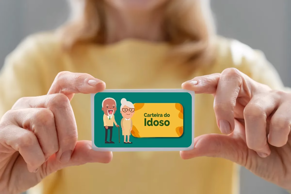 Pessoa segurando uma Carteira do Idoso com ilustração colorida.