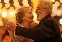 Casal de idosos dançando juntos, rodeados por luzes festivas e sorrindo, em uma celebração social.