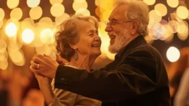 Casal de idosos dançando juntos, rodeados por luzes festivas e sorrindo, em uma celebração social.