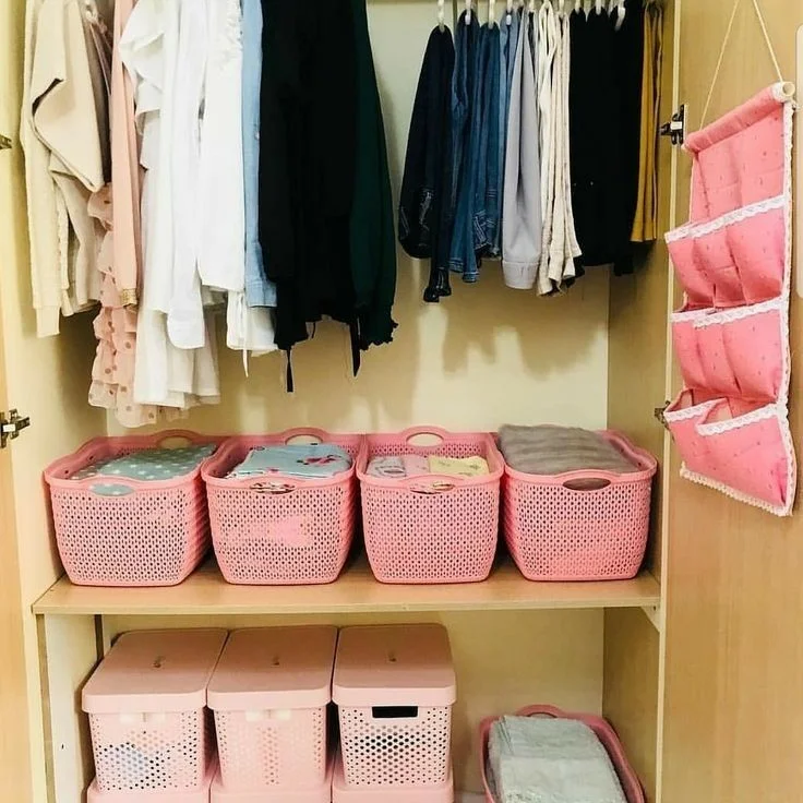 Cestos e caixas organizando acessórios de inverno no armário, com roupas penduradas ao fundo.