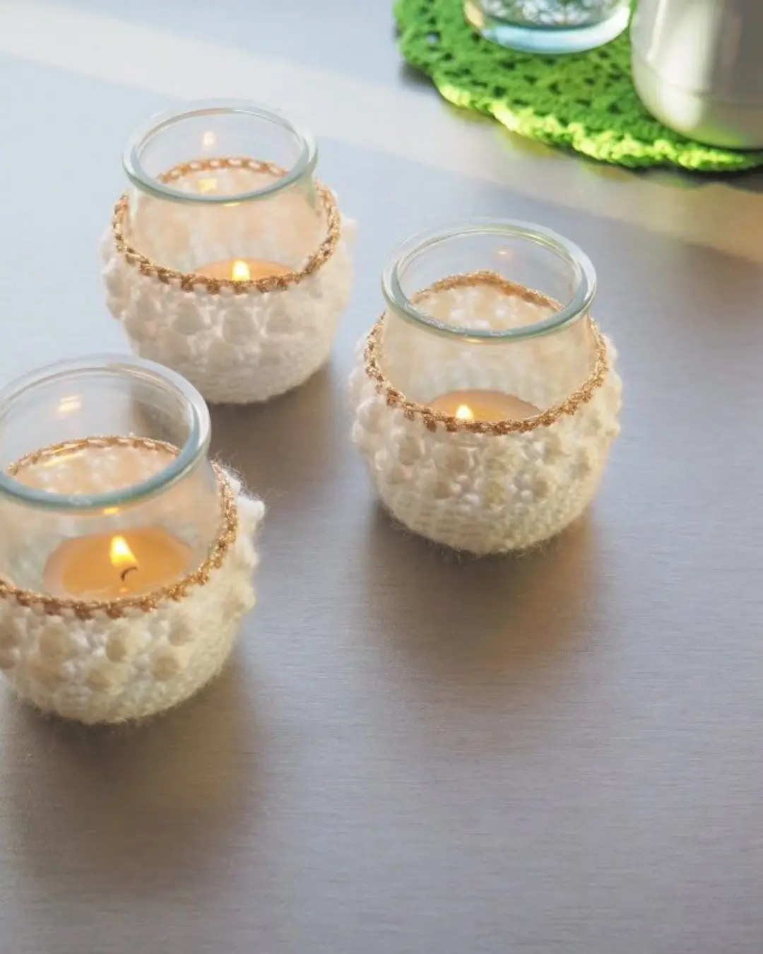 Luminárias feitas com vidro e crochê, com velas acesas no centro, em um ambiente tranquilo e acolhedor.