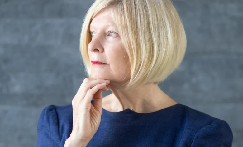 Mulher madura com cabelo chanel elegante, vestindo um vestido azul, olhando para o futuro com expressão pensativa. O corte de cabelo chanel traz sofisticação e modernidade.