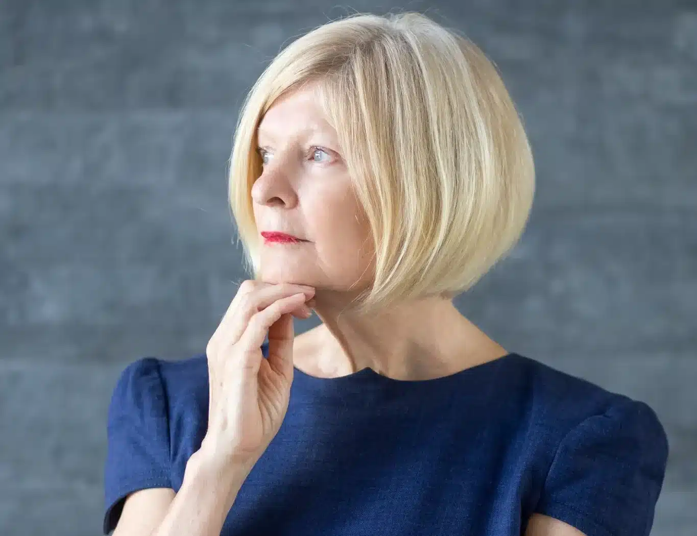 Mulher madura com cabelo chanel elegante, vestindo um vestido azul, olhando para o futuro com expressão pensativa. O corte de cabelo chanel traz sofisticação e modernidade.