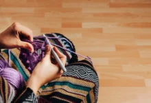 Mãos trabalhando em um projeto de crochê para tapete com fio roxo em um ambiente aconchegante.