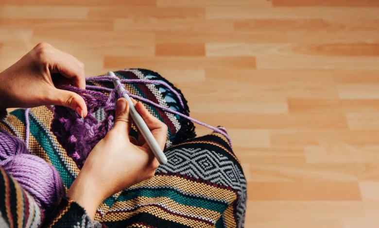 Mãos trabalhando em um projeto de crochê para tapete com fio roxo em um ambiente aconchegante.