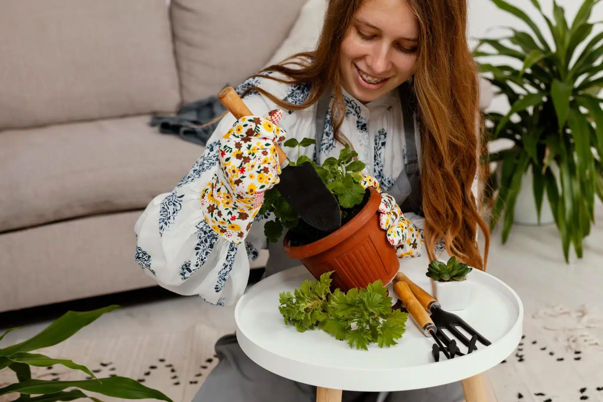 Mulher sorridente plantando em casa com ferramentas de jardinagem e vaso de planta em um ambiente aconchegante.