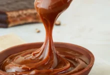 Colher derramando doce de leite cremoso em tigela de madeira