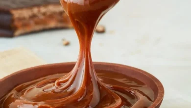 Colher derramando doce de leite cremoso em tigela de madeira