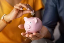 Pessoa colocando moeda em cofre de porquinho rosa, representando economia doméstica.