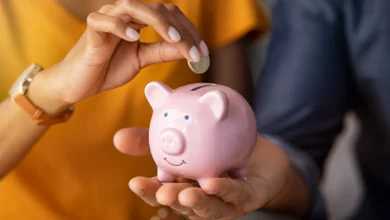 Pessoa colocando moeda em cofre de porquinho rosa, representando economia doméstica.