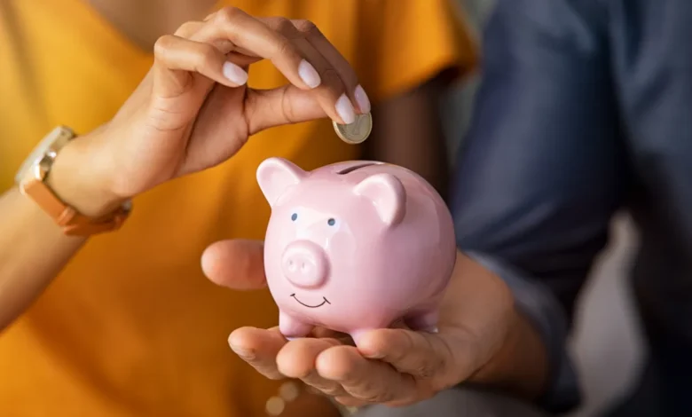 Pessoa colocando moeda em cofre de porquinho rosa, representando economia doméstica.