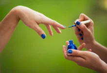Mulher aplicando esmalte vegano azul em outra mulher em ambiente natural.